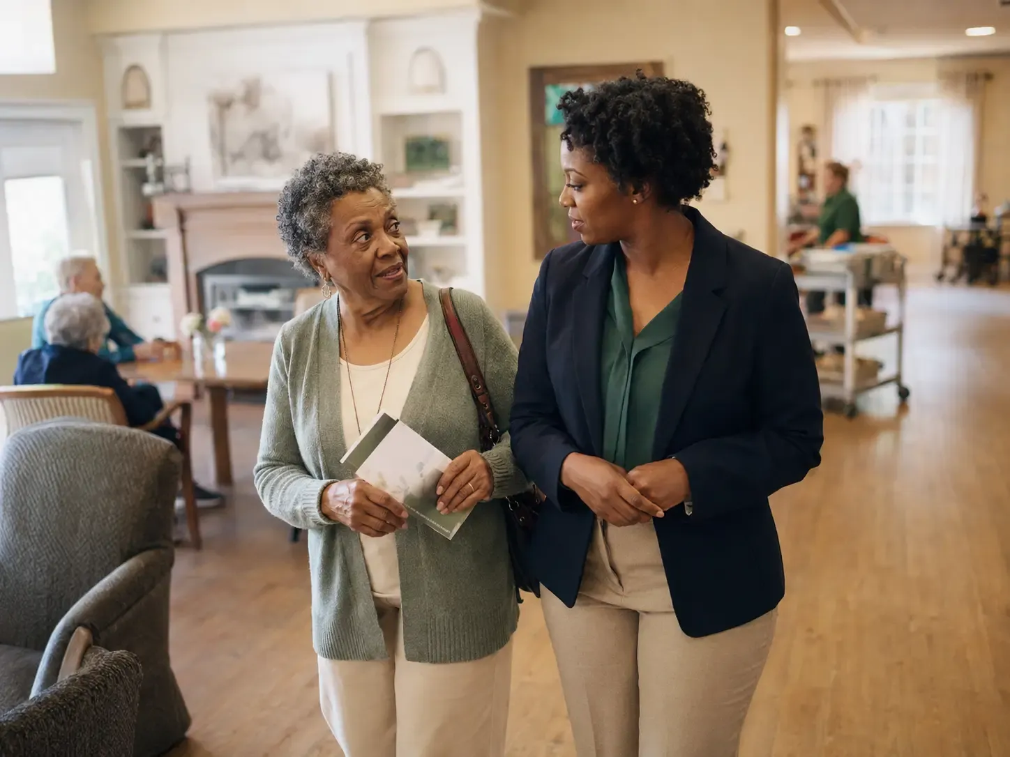 A Black senior woman walking through an assisted living common area with an admissions professional