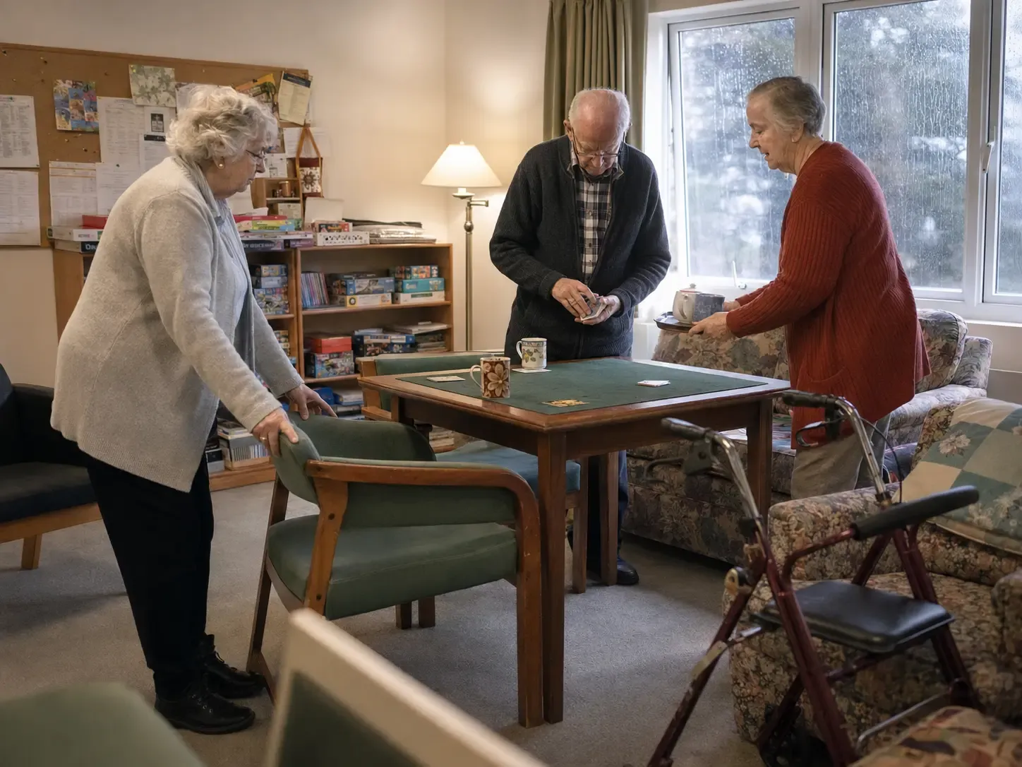 Three independent living residents setting up a card game on a rainy afternoon
