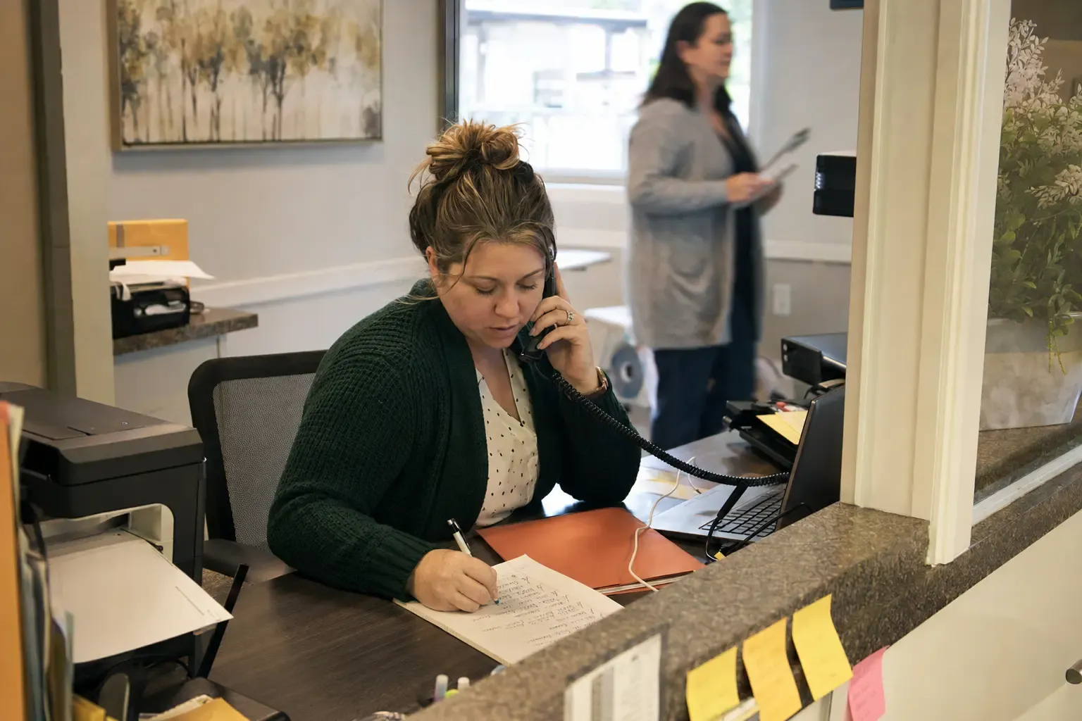 A senior living admissions coordinator returning a family call from a busy reception back desk
